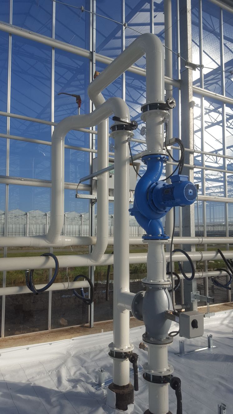 Verwarmingsmanifold met wit geverfde staande leidingen en een blauwe pomp